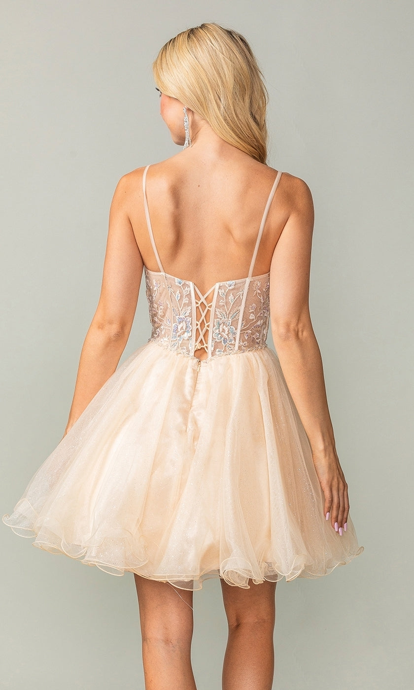 A woman with long blonde hair models the Lace-Up Short Babydoll Homecoming Dress 3352, a sleeveless light peach party dress with a corset-style bodice, sheer embroidery, and lace-up back, standing against a plain background.